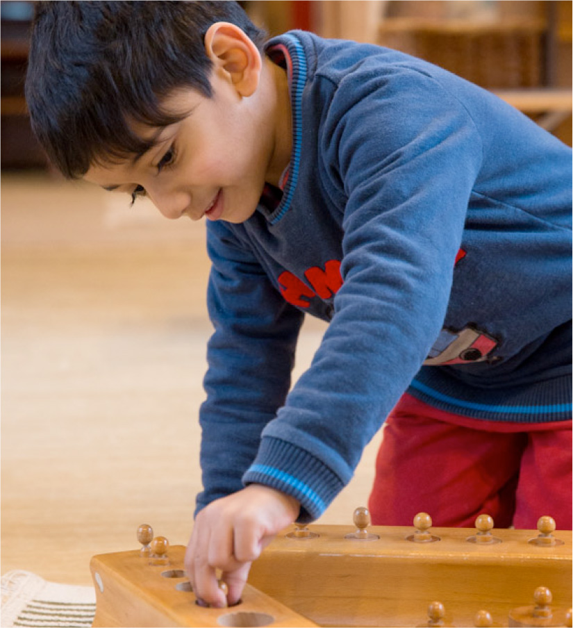 Smiling boy playing with wooden pegs (Grantham Farm Montessori School)