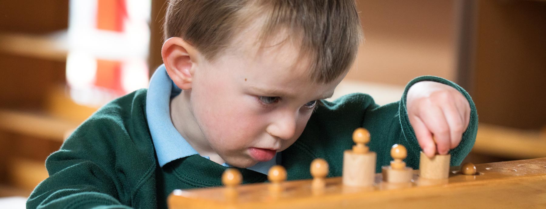 Young child focused on putting pegs into holes (Grantham Farm Montessori School)