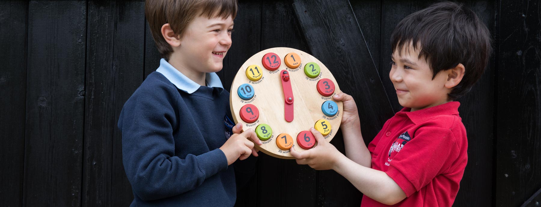 Two kids smiling at each other as they hold up a colourful clock between them (Grantham Farm Montessori School)