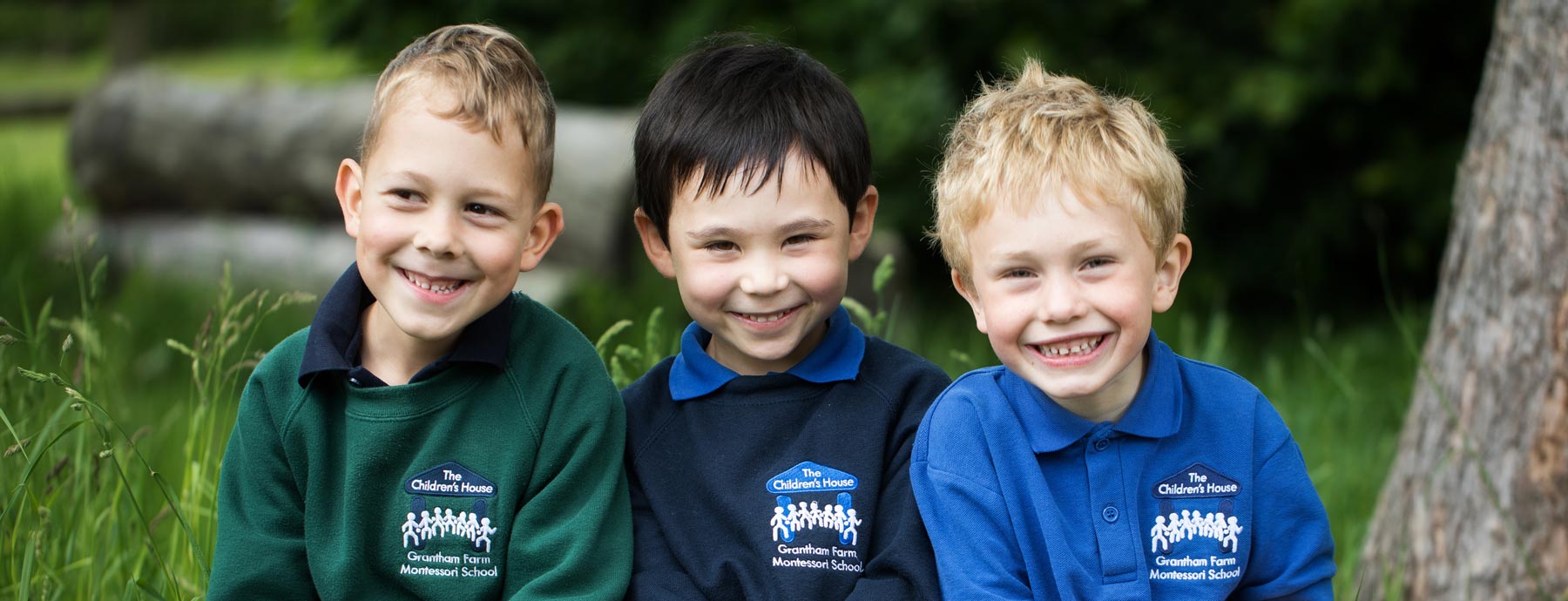 Three smiling children wearing different colours of our school uniform (Grantham Farm Montessori School)