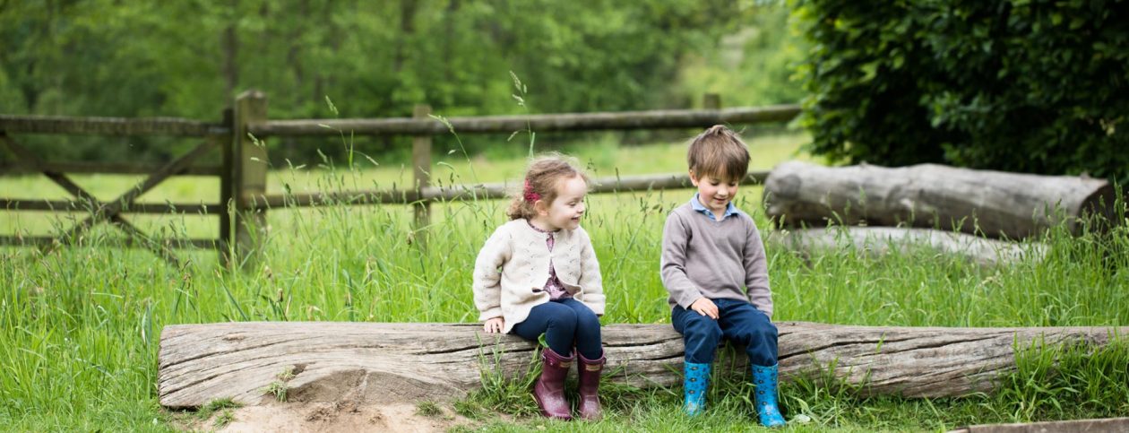 Two happy children sitting on a log outdoors (Grantham Farm Montessori School)