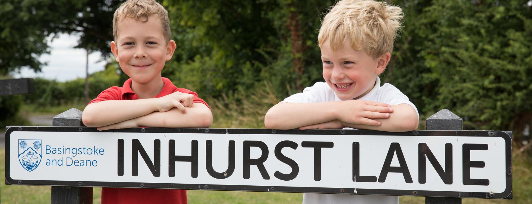 Two smiling children behind the road sign for Inhurst Lane (Grantham Farm Montessori School)